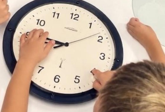 Children moving the hands of a wall clock together on a table